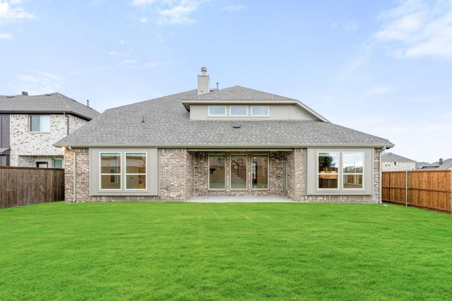 Rear exterior of brick home with large windows, patio door, and fenced backyard with green lawn Rear exterior of brick home with large windows, patio door, and fenced backyard with green lawn