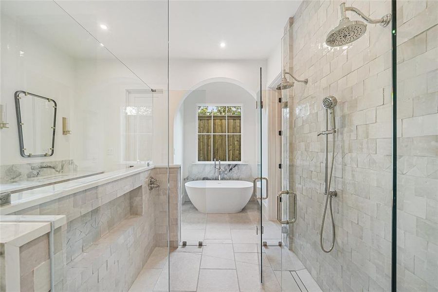 Spacious bathroom featuring a freestanding soaking tub, a large walk-in shower with multiple showerheads, and a double vanity with a marble-patterned countertop