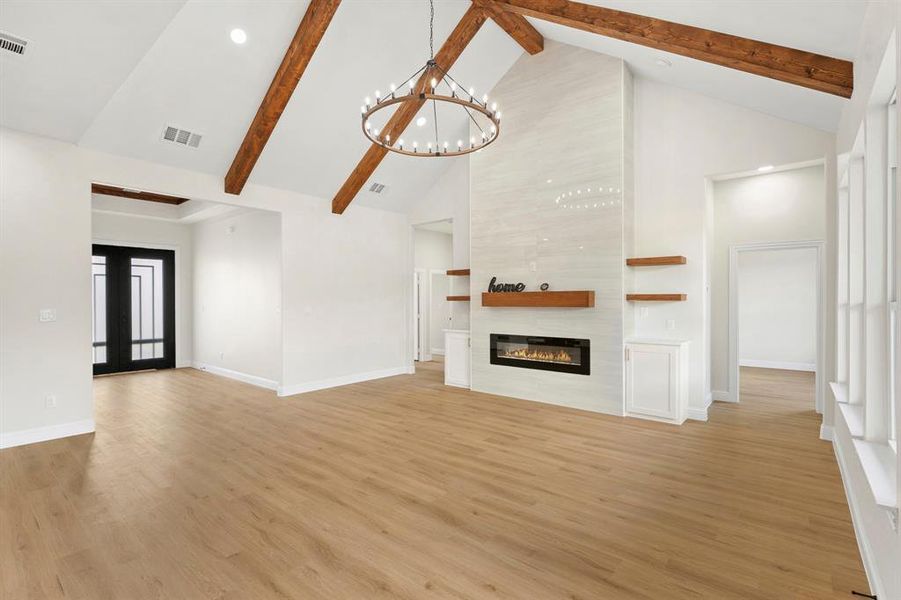 Unfurnished living room featuring beam ceiling, high vaulted ceiling, a large fireplace, light wood finished floors, and french doors