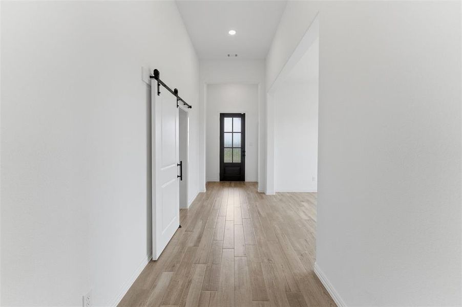 This bright hallway features light wood-look flooring, recessed lighting, and a modern barn door