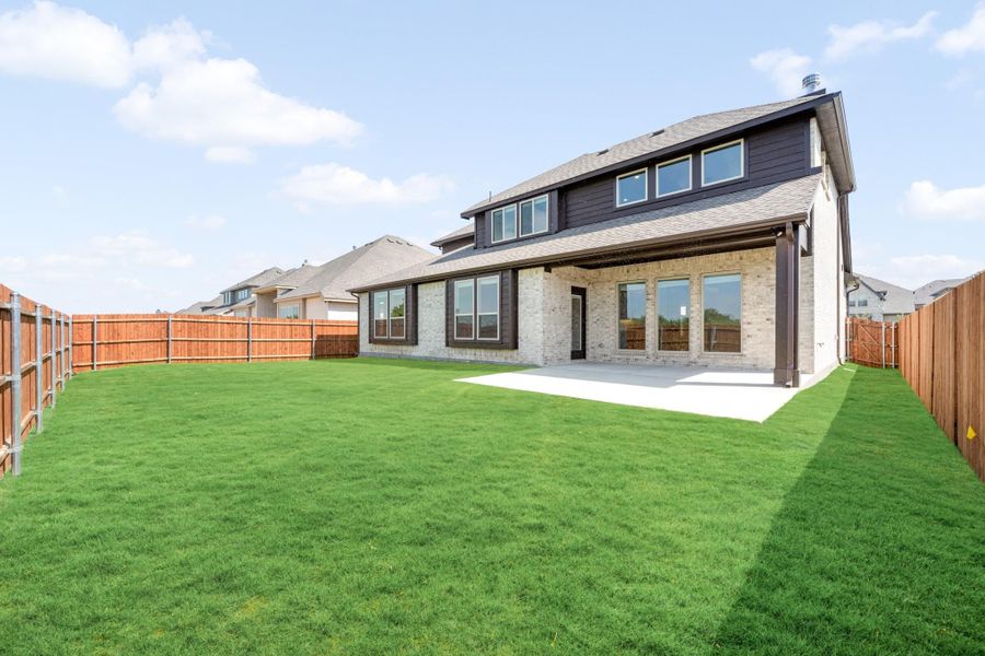 Two-story brick home with dark siding, covered back patio, large grassy yard, and wood privacy fence.