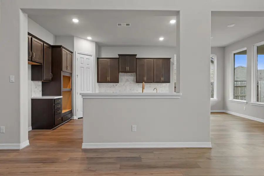 This light and bright kitchen features a large quartz island, dark stained cabinets, a large sink overlooking your family room, recessed lighting, and beautiful backsplash.