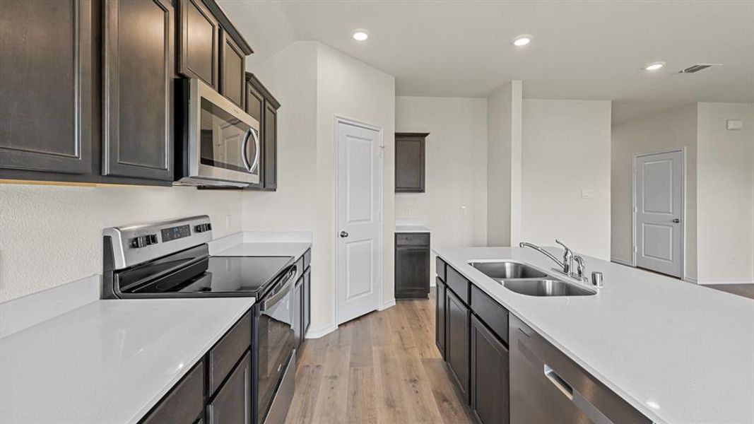 Kitchen with stainless steel appliances, light wood-type flooring, recessed lighting, light stone countertops, and dark wood finish cabinets