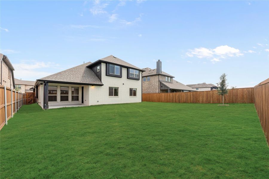 Backyard of two-story home with large green lawn, covered patio, and wood privacy fence