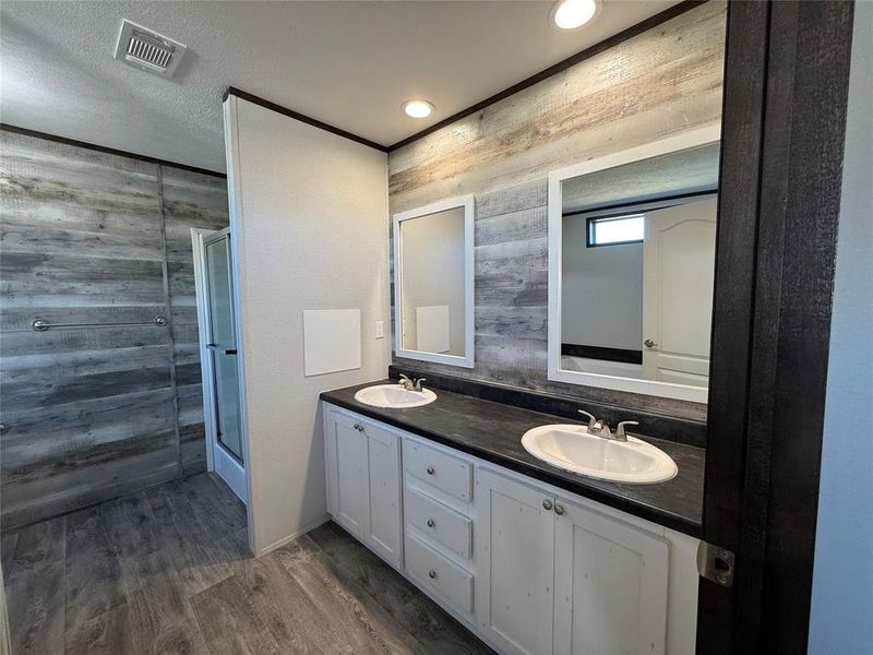Bathroom featuring wood walls, dark wood-style floors, double vanity, a stall shower, and a textured ceiling