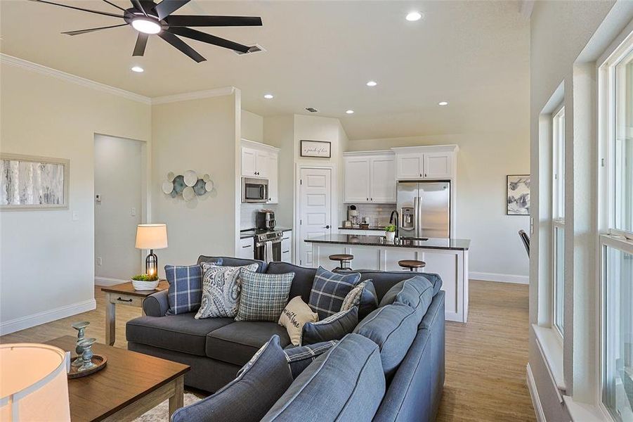 Open-concept living area featuring a kitchen island with seating, recessed lighting, wood-finish flooring, and multiple large windows