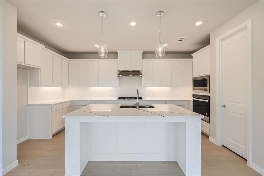 Kitchen featuring a kitchen island with sink, light hardwood / wood-style flooring, hanging light fixtures, white cabinets, and appliances with stainless steel finishes