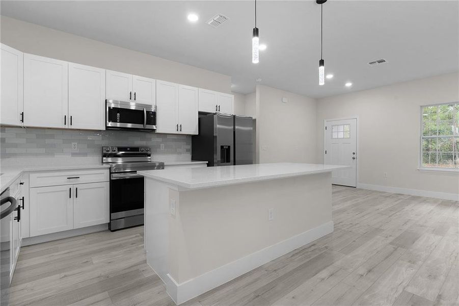 Beautiful kitchen with stainless steel Samsung appliances, tiled backsplash, and kitchen island with breakfast bar