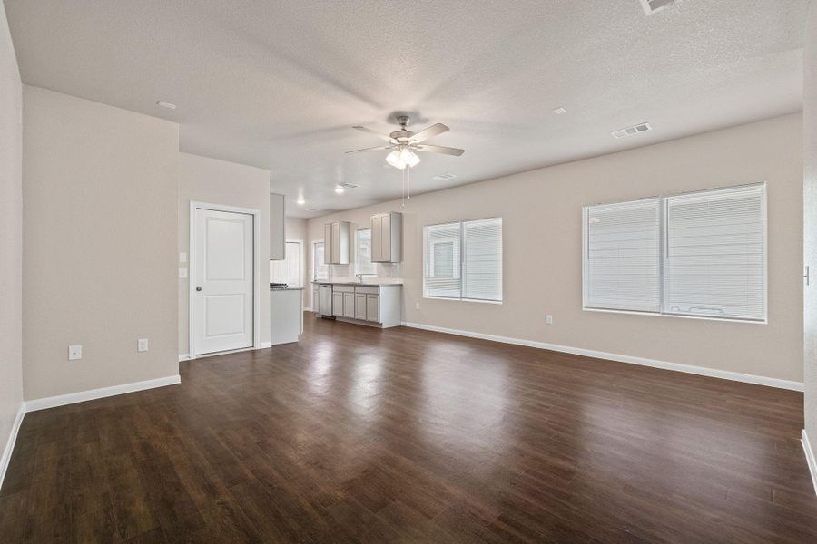 Unfurnished living room featuring a ceiling fan, dark wood-style flooring, and a textured ceiling