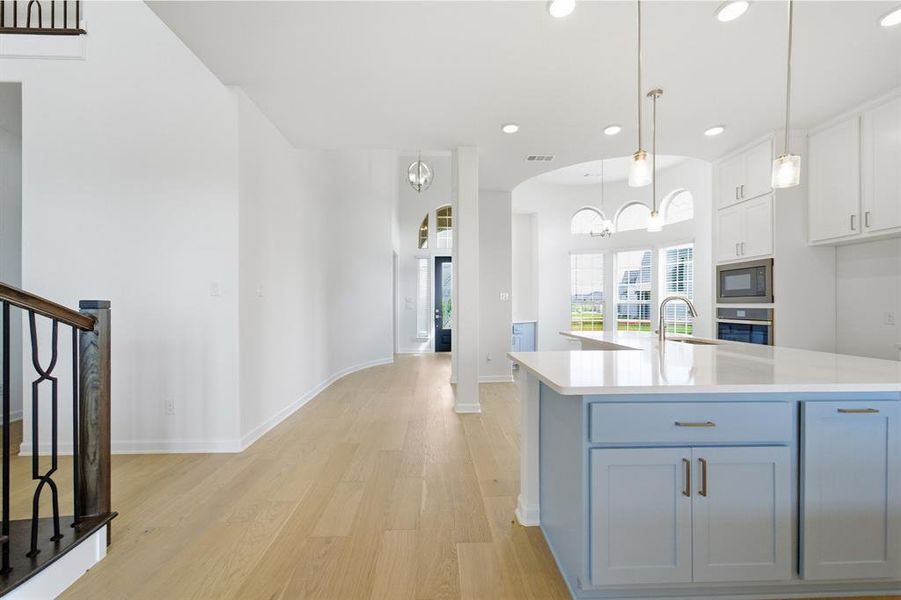 Open-concept kitchen featuring a light blue island with a white countertop, stainless steel appliances, and pendant lighting