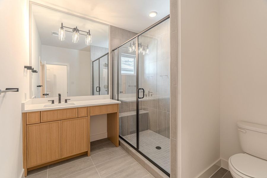 This modern bathroom features a spacious glass-enclosed shower, a sleek vanity with ample storage, and contemporary lighting. Neutral tones create a clean, stylish look.