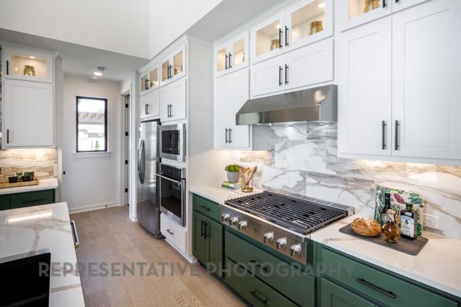 Kitchen featuring under cabinet range hood, white cabinets, stainless steel appliances, and green cabinets Kitchen featuring under cabinet range hood, white cabinets, stainless steel appliances, and green cabinets