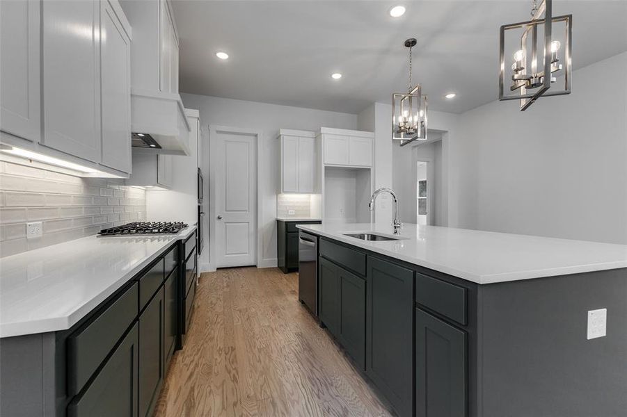 Kitchen featuring tasteful backsplash, white cabinets, a center island with sink, sink, and light wood-type flooring