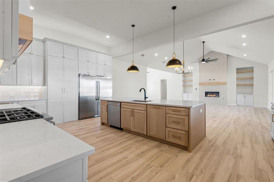 Kitchen featuring a fireplace, lofted ceiling, decorative light fixtures, stainless steel appliances, and light wood finished floors Kitchen featuring a fireplace, lofted ceiling, decorative light fixtures, stainless steel appliances, and light wood finished floors