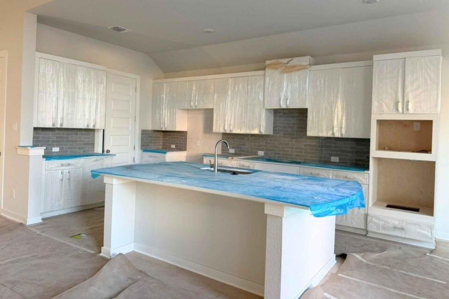 Kitchen featuring an island with sink, backsplash, a breakfast bar, lofted ceiling, and light countertops