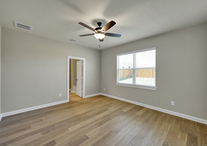 Spacious primary bedroom featuring a ceiling fan, wood-look flooring, and a window with natural light.