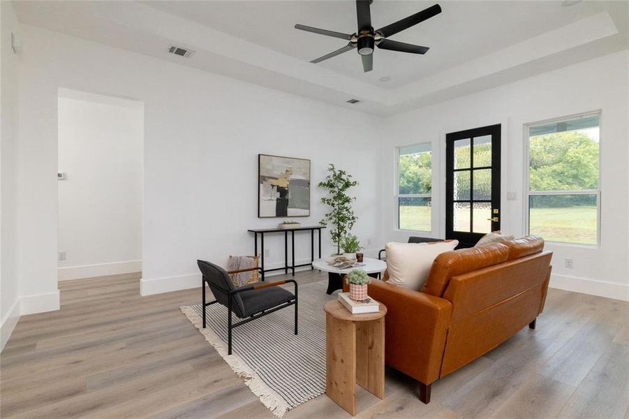 Living room featuring ceiling fan, a raised ceiling, and light wood-type flooring