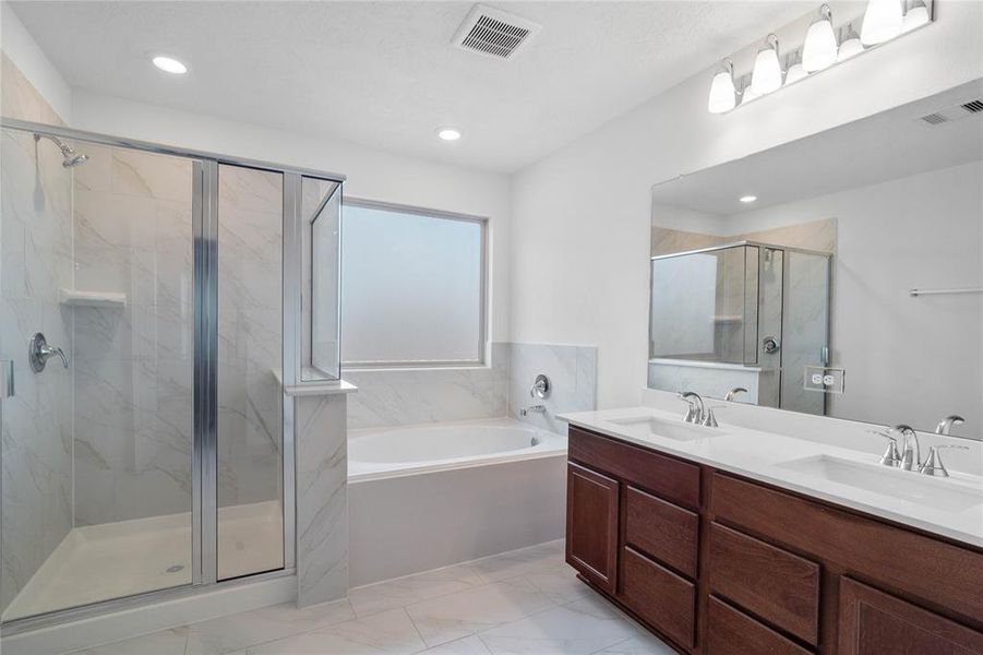 This primary bathroom is definitely move-in ready! Featuring a dark framed walk-in shower with tile surround, separate garden tub for soaking after a long day with custom tile detailing, stained cabinets with light countertops and dual vanities, high ceilings, recessed lighting, custom paint, sleek and dark modern finishes.