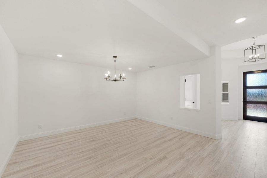 Empty dining room with light wood floors, white walls, and a chandelier near the entryway