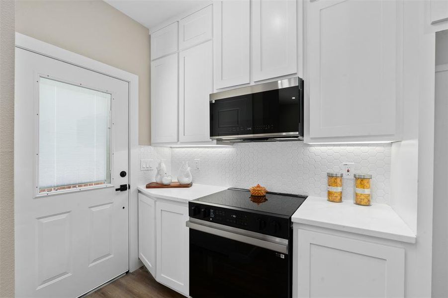 Kitchen featuring black range with electric stovetop, backsplash, white cabinetry, and stainless steel microwave