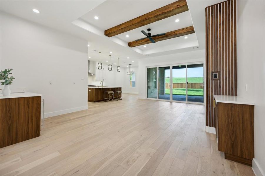 Unfurnished living room featuring beamed ceiling, light wood-type flooring, and ceiling fan