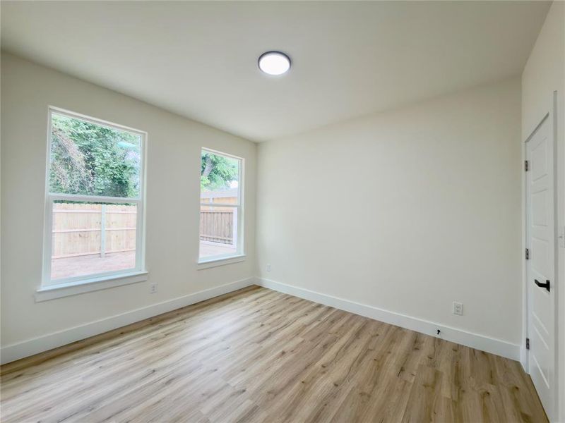 Room featuring wood-finish flooring, white baseboards, two windows with white trim, and a ceiling-mounted light fixture