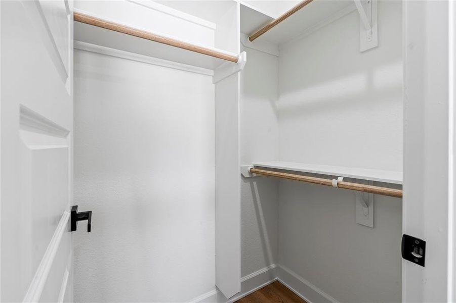 Spacious walk-in closet with sturdy wooden rods and ample shelving, perfect for organized storage. Spacious walk-in closet with sturdy wooden rods and ample shelving, perfect for organized storage.
