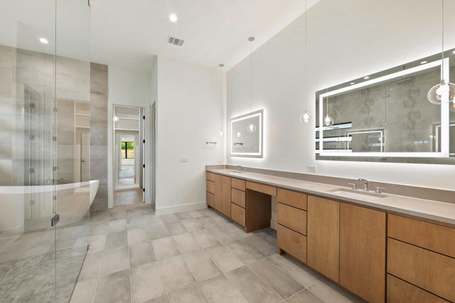 Bathroom featuring a freestanding tub, glass-enclosed shower, dual vanity with undermount sinks, wood-finish cabinetry, and illuminated mirrors