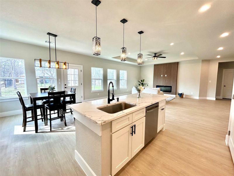 Kitchen with light stone counters, decorative light fixtures, light wood-type flooring, stainless steel dishwasher, and white cabinets