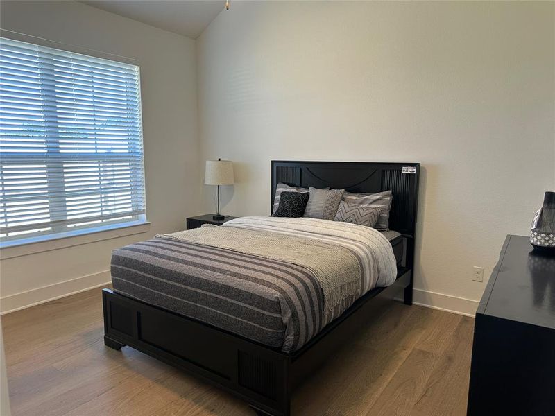 Room featuring wood-finish flooring, a vaulted ceiling, and ample natural light from a large window with blinds