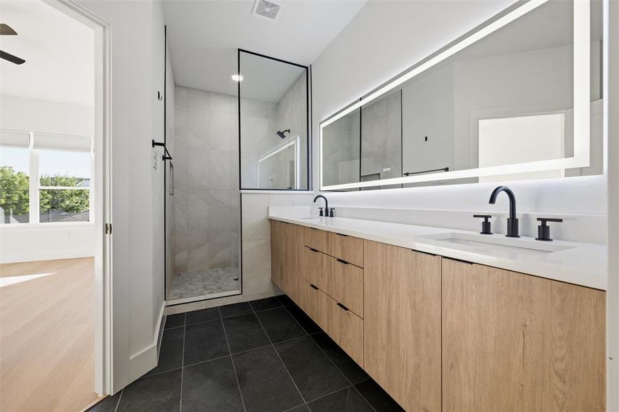 Primary Bathroom features recessed lighting. Walkin shower includes glass enclosure and large- format tile surround. Extended wood vanity provides dual sinks, quartz countertops, and black fixtures. Tile flooring extends throughout.