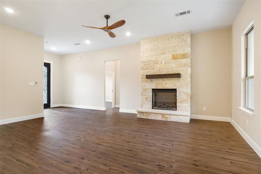 Unfurnished living room featuring ceiling fan, dark hardwood / wood-style floors, and a stone fireplace