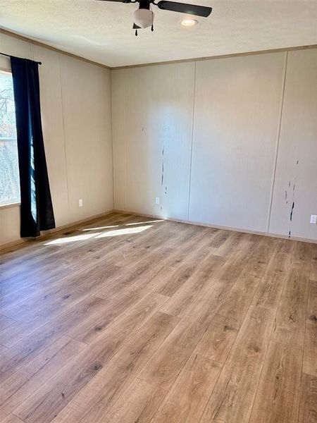 Unfurnished room with a decorative wall, light wood-type flooring, ceiling fan, and a textured ceiling Unfurnished room with a decorative wall, light wood-type flooring, ceiling fan, and a textured ceiling