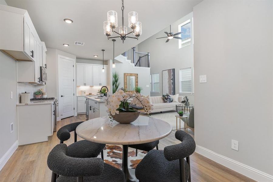 Dining area with ceiling fan with notable chandelier, a high ceiling, light wood-type flooring, and sink