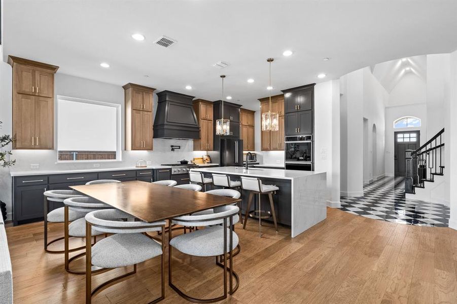 Kitchen with an island with sink, a kitchen breakfast bar, light wood finished floors, decorative light fixtures, and custom range hood Kitchen with an island with sink, a kitchen breakfast bar, light wood finished floors, decorative light fixtures, and custom range hood