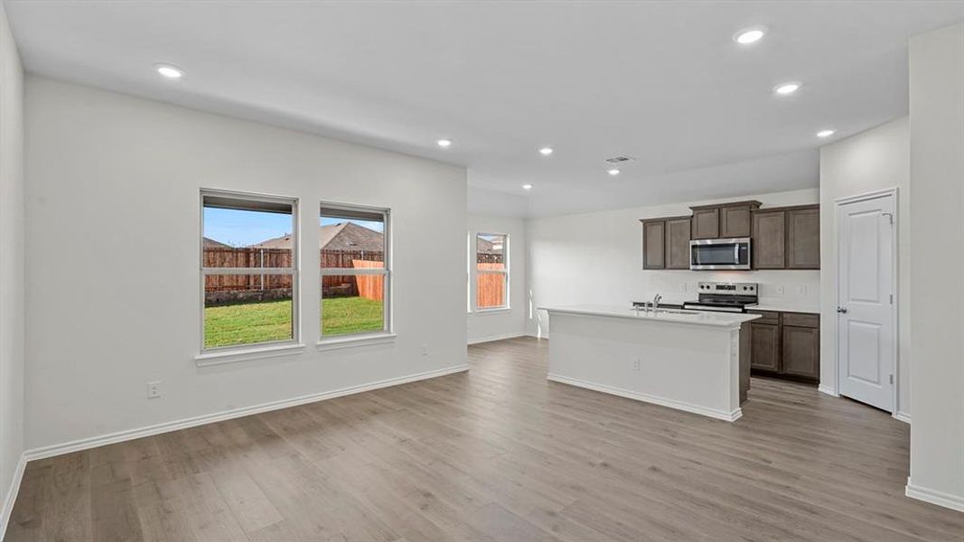 Kitchen with a center island with sink, stainless steel appliances, dark wood finish cabinetry, light wood-type flooring, and open floor plan