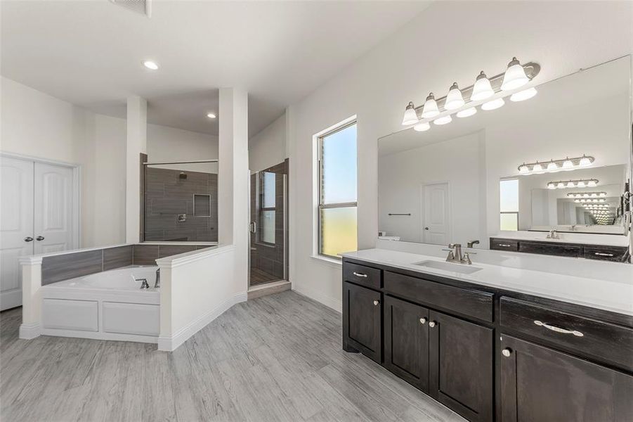 Full bath with wood finished floors, a stall shower, a bath, vanity, and baseboards
