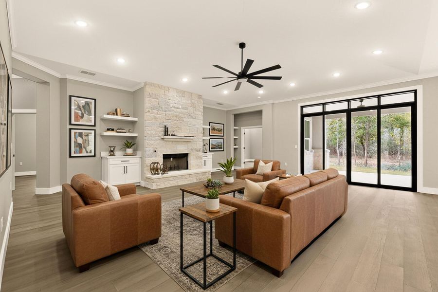 Living room featuring crown molding, built in shelves, a fireplace, wood floors, and ceiling fan, virtually staged Living room featuring crown molding, built in shelves, a fireplace, wood floors, and ceiling fan, virtually staged