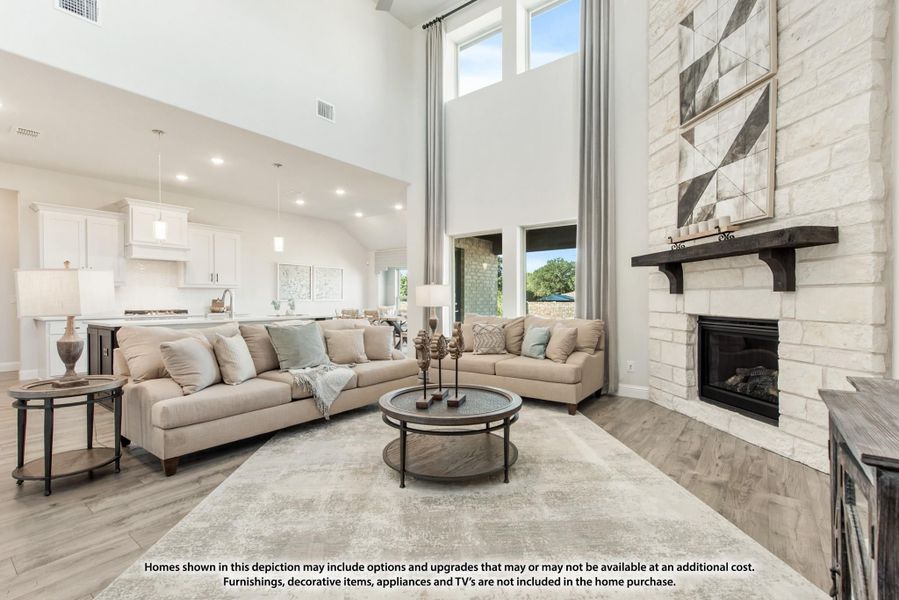 Open living room with two-story ceiling, stone fireplace, and open kitchen in background