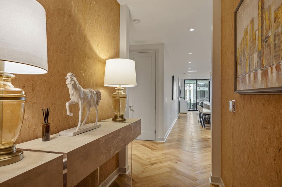 Herringbone hardwood floors extend through this naturally illuminated hallway, leading to an open living area.