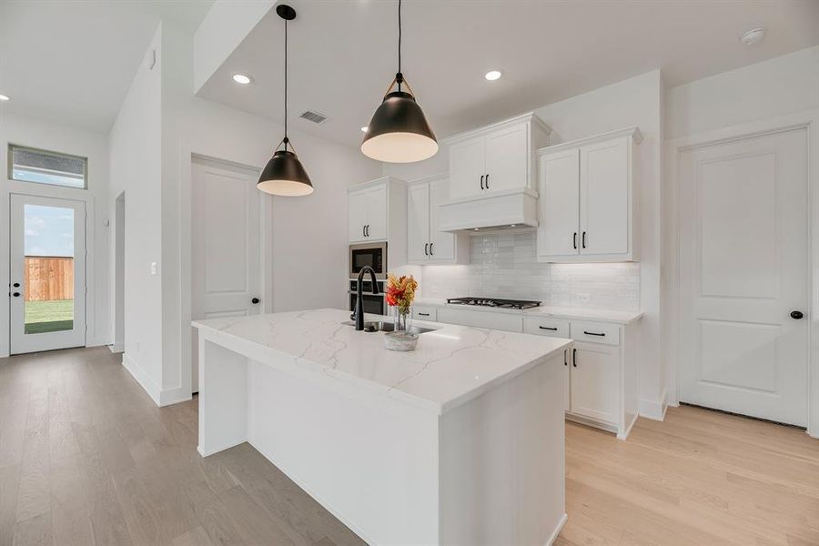 Kitchen with decorative backsplash, white cabinetry, a center island with sink, light wood-style floors, and recessed lighting Kitchen with decorative backsplash, white cabinetry, a center island with sink, light wood-style floors, and recessed lighting