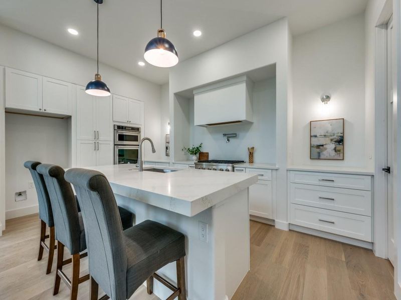 Kitchen with hanging light fixtures, sink, and white cabinets