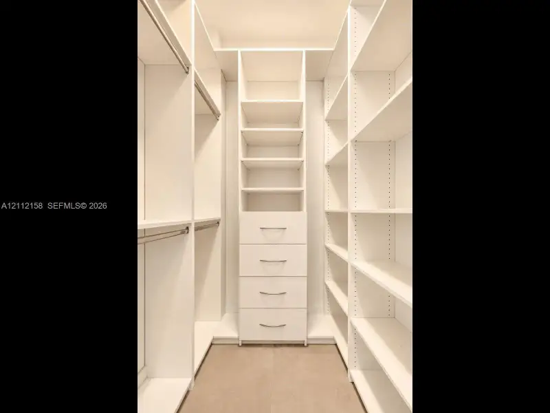 Organized walk-in closet with custom white built-ins, hanging rods, adjustable shelving, and a built-in four-drawer dresser