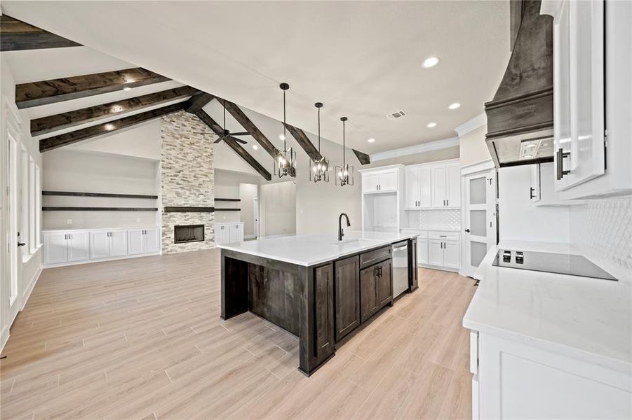 Kitchen featuring white cabinetry, light stone countertops, dark brown cabinetry, a center island with sink, and wood tiled floors