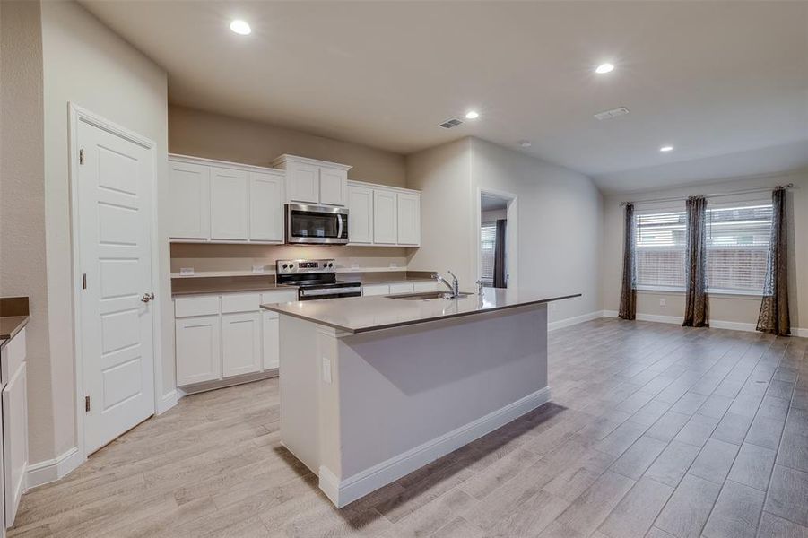 Kitchen with recessed lighting, stainless steel appliances, an island with sink, white cabinetry, and light wood-style floors Kitchen with recessed lighting, stainless steel appliances, an island with sink, white cabinetry, and light wood-style floors