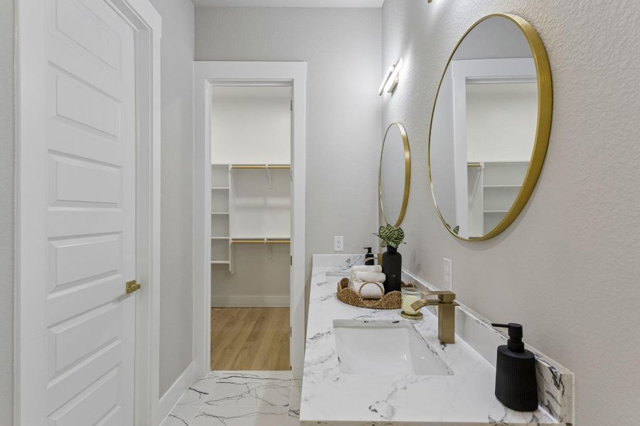 A well-appointed vanity with dual sinks, gold-framed mirrors, and a spacious walk-in closet beyond.