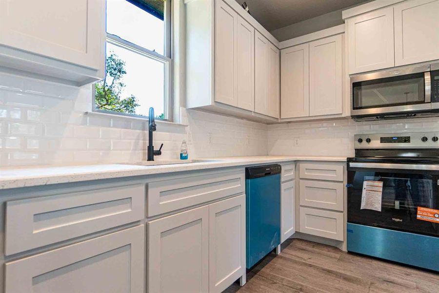 Kitchen with appliances with stainless steel finishes, tasteful backsplash, dark wood-type flooring, and white cabinets