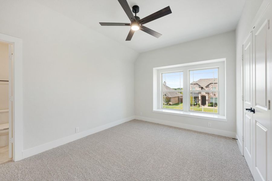 Empty bedroom with vaulted ceiling, ceiling fan, carpet flooring, and large window with neighborhood view