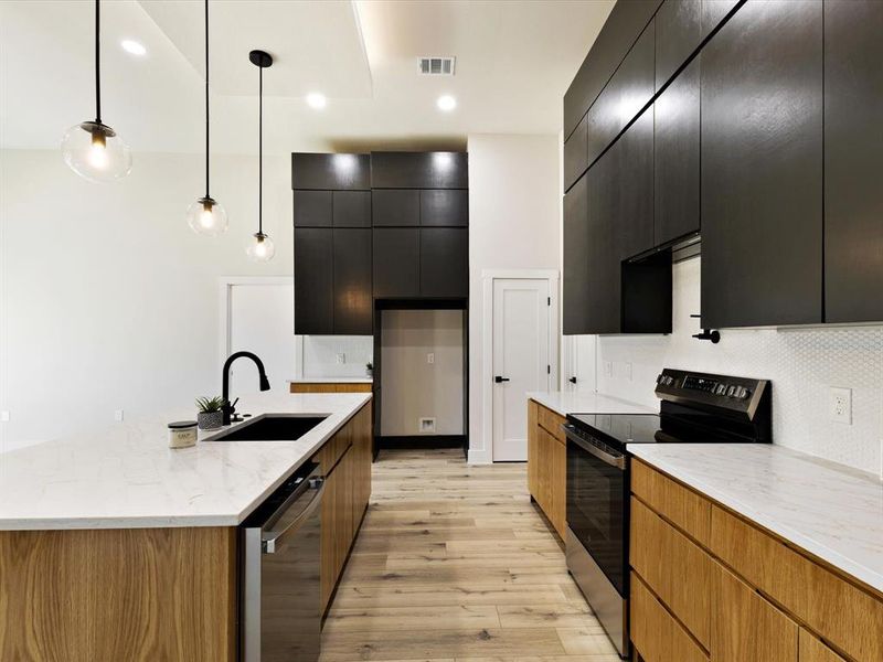 Kitchen with black / electric stove, light stone countertops, stainless steel dishwasher, decorative light fixtures, and modern cabinets