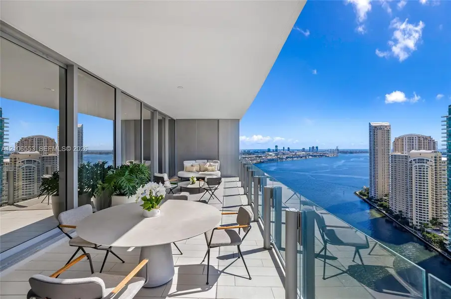 Expansive covered balcony featuring large-format tile flooring, recessed ceiling lighting, and a floor-to-ceiling glass railing